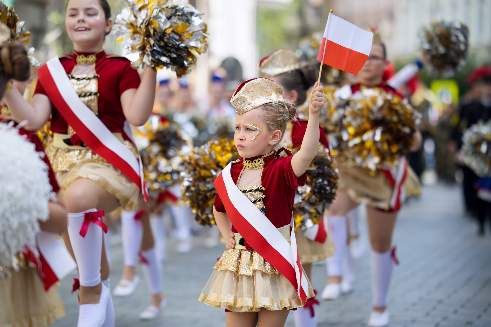 dziewczynki w biało-czerwonych strojach z flagami idą ulicą w paradzie