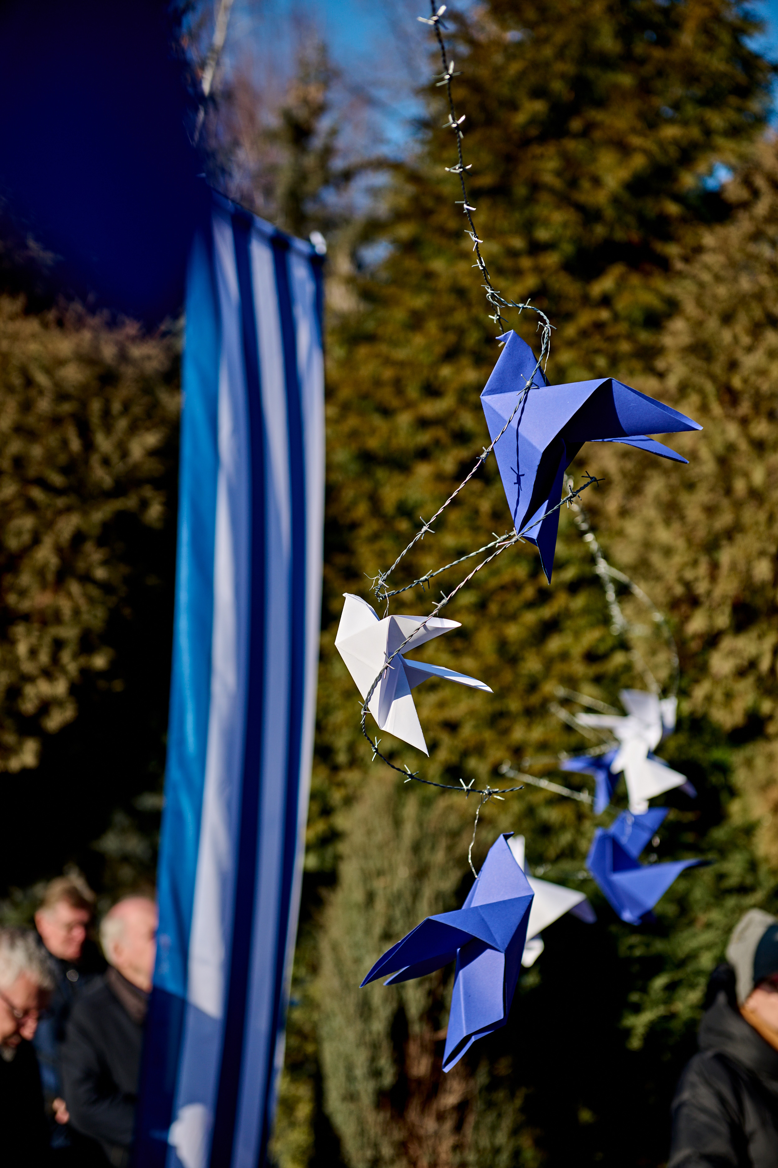 Gołębie z origami wiszące na drutach kolczastych nad mogiłami