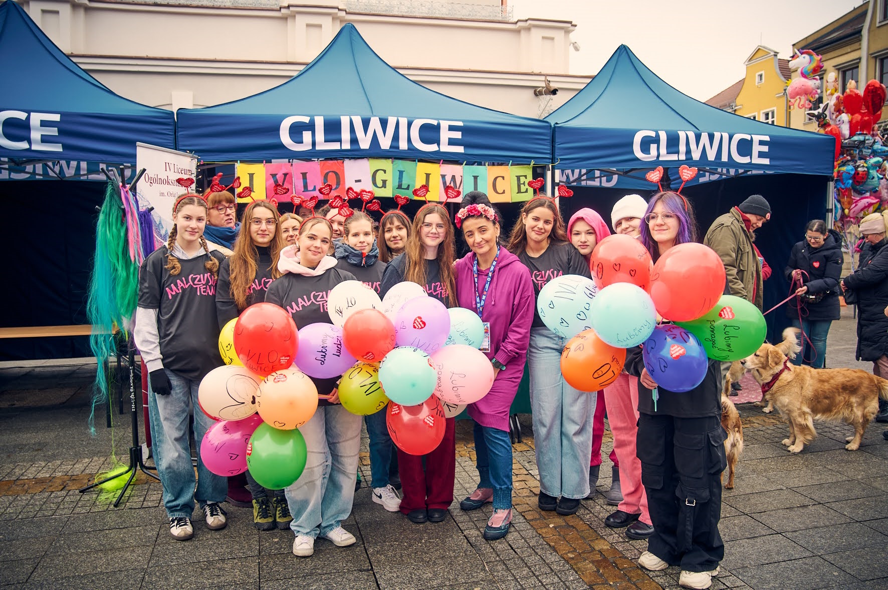 Uczniowie i nauczycielka z kolorowymi balonami przy stoisku z napisem Gliwice