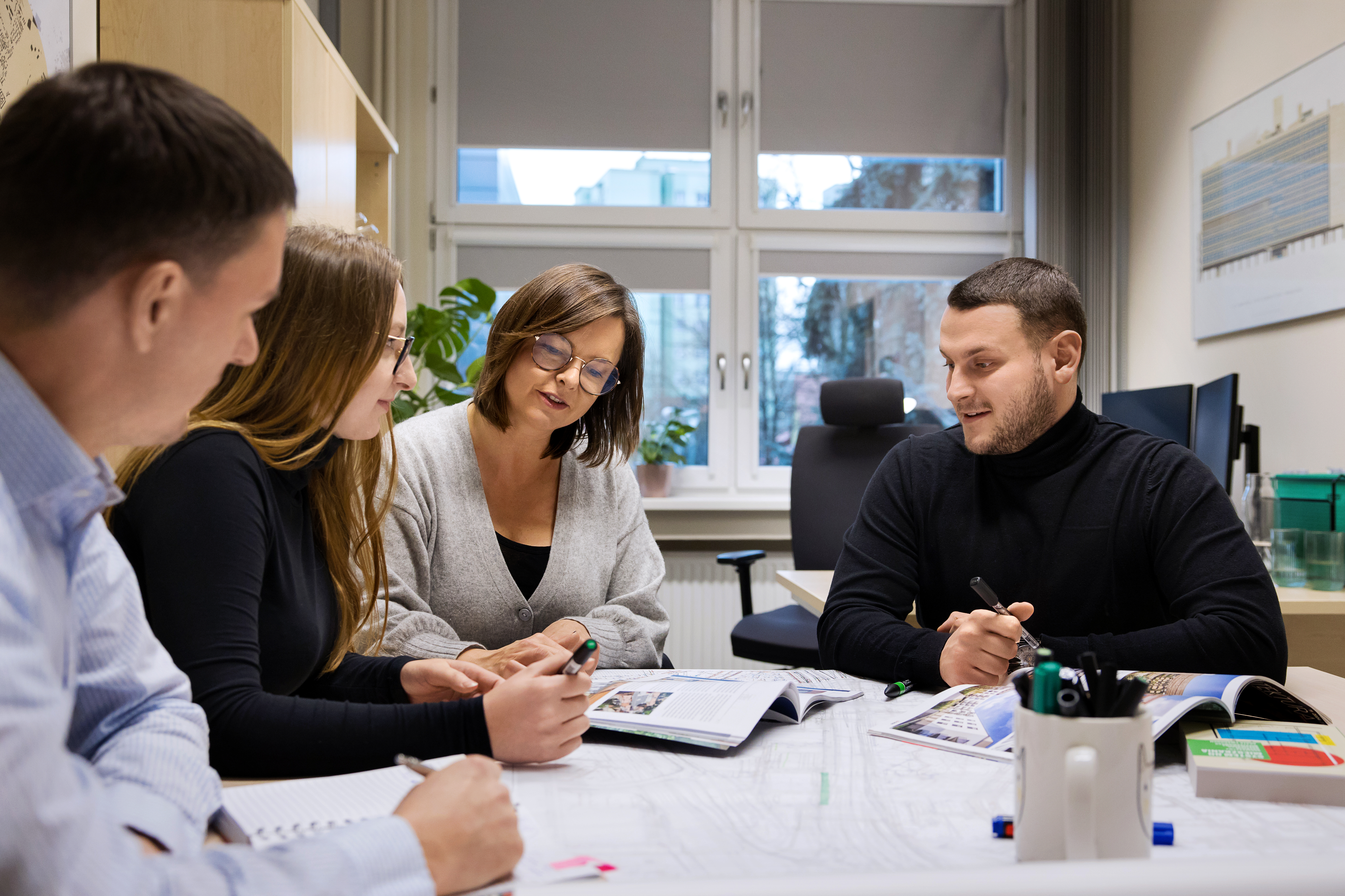 Czterech członków biura siedzących przy stole z projektami