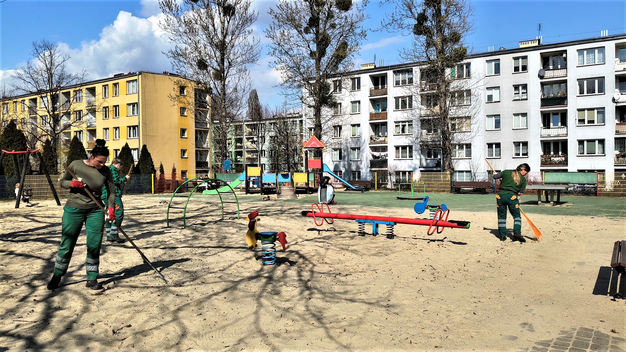trzy kobiety grabią piasek na placu zabawa