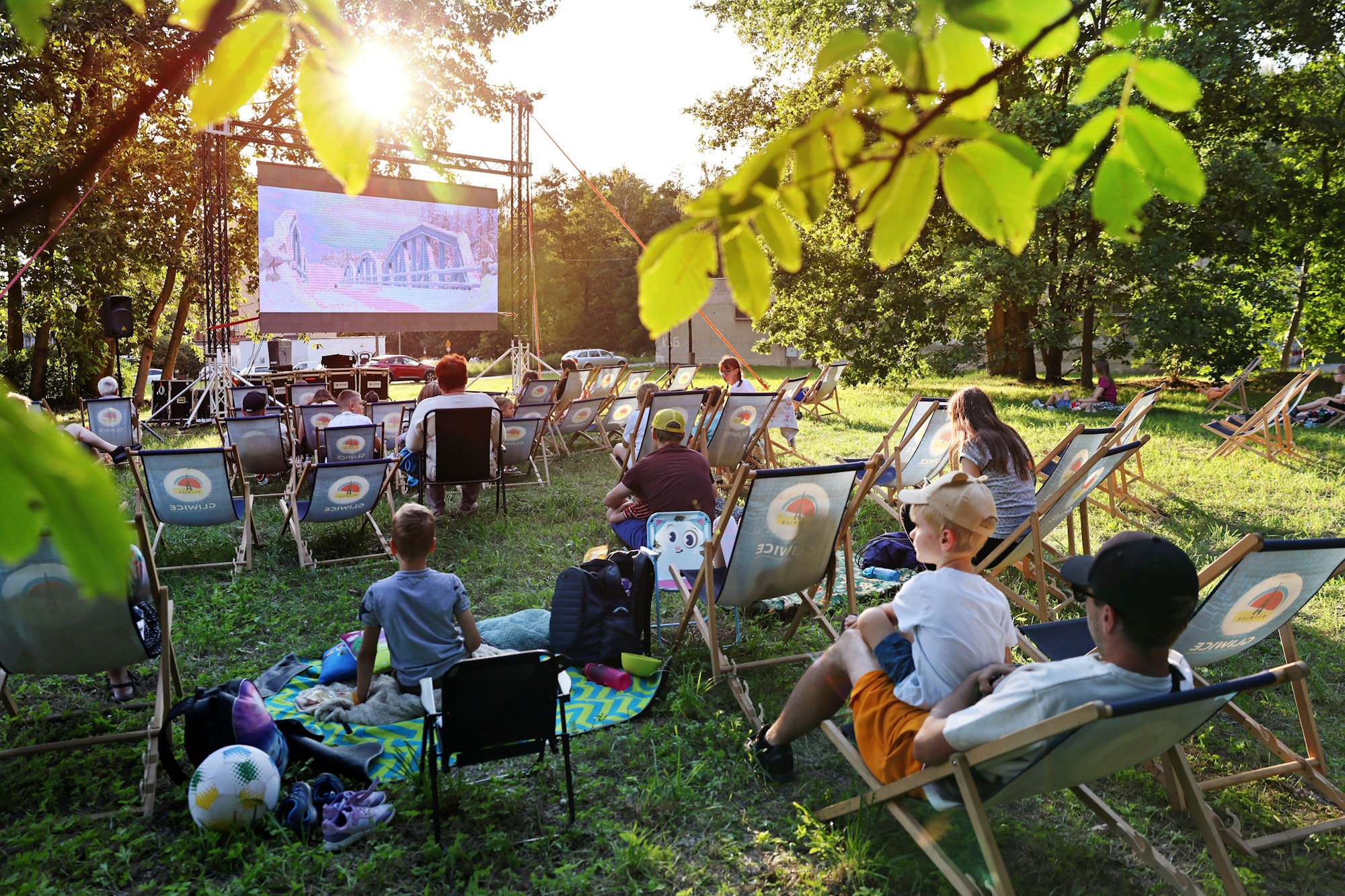 Ludzie siedzą w parku i oglądają film wyświetlony na rzutniku