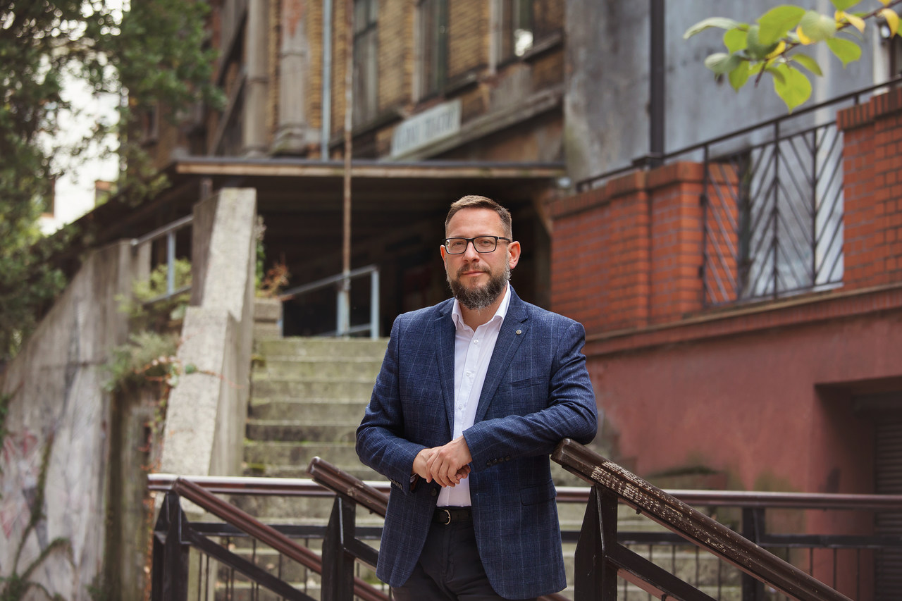 elegancki mężczyzna opiera się o balustradę przed ruinami teatru Victoria